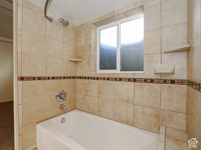 Tiled shower surround with decorative accent border, built-in shelving, sliding window, and chrome plumbing fixtures