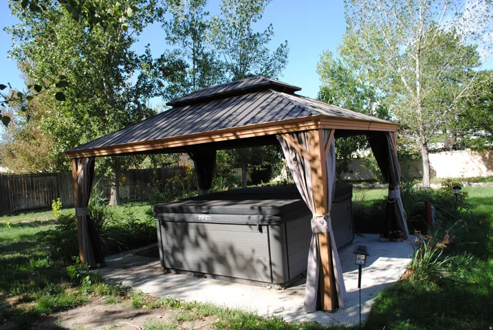 Backyard gazebo with a tiered roof, a hot tub, and concrete hardscaping