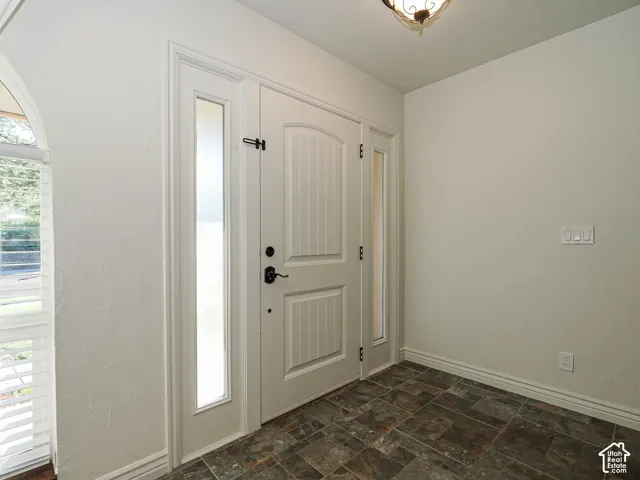 Entryway featuring a paneled door with dual sidelights, stone-finish tile flooring, an arched window, and a ceiling-mounted light fixture