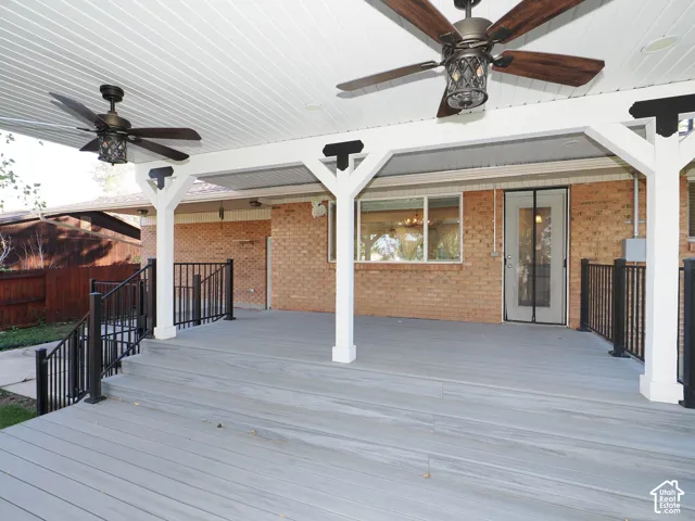 Covered outdoor deck featuring composite decking, dual ceiling fans, white support columns with decorative brackets, and black metal railings