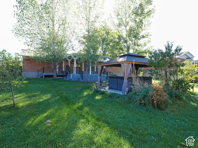 Expansive backyard featuring a brick exterior, elevated rear deck with black metal railing, and a hardscaped gazebo covering a built-in spa