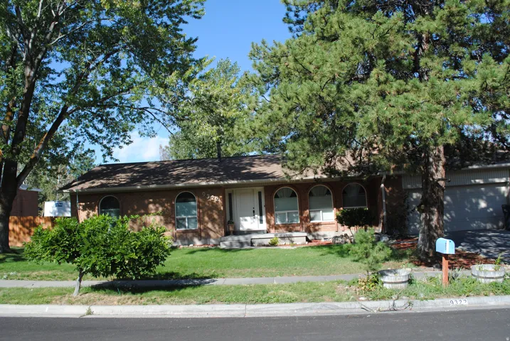 Brick exterior with arched windows, prominent mature trees, an attached garage, a white front entry door, and a grass lawn