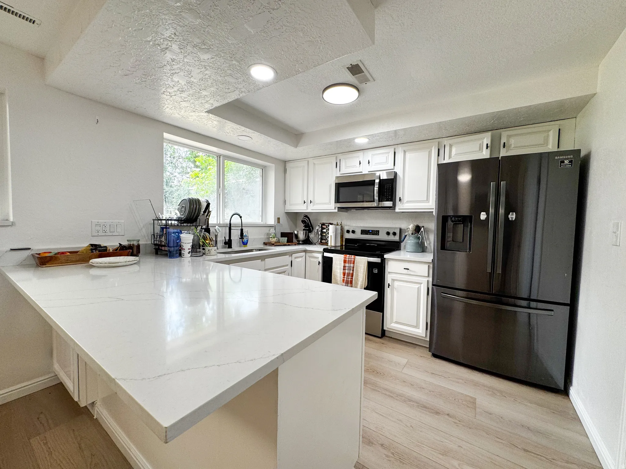 Kitchen featuring white cabinetry, light-toned wood-finish flooring, white countertop surfaces, and stainless-steel appliances
