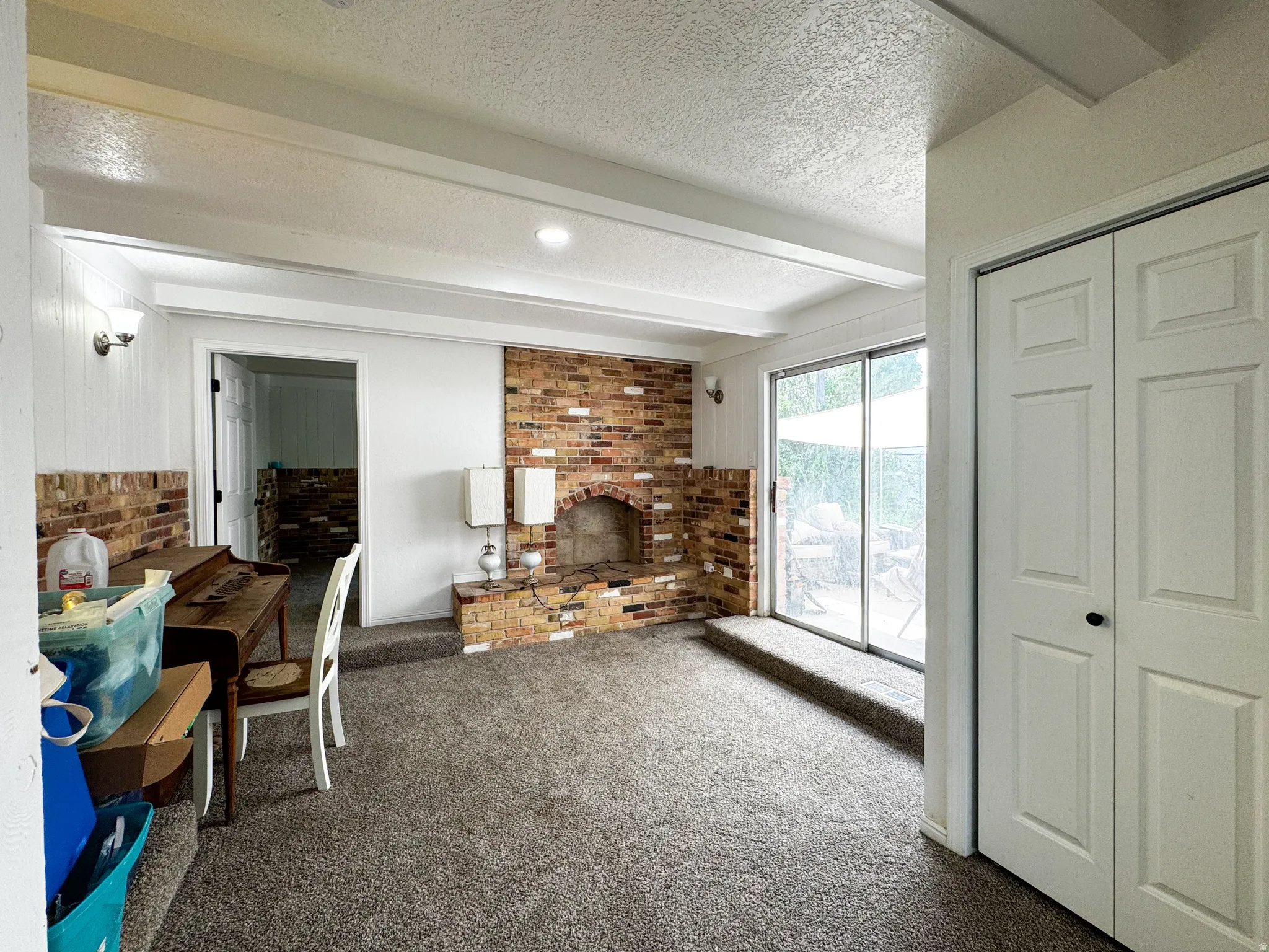 Exposed brick fireplace, sliding glass door, white bi-fold closet doors, wall paneling, and ceiling beams
