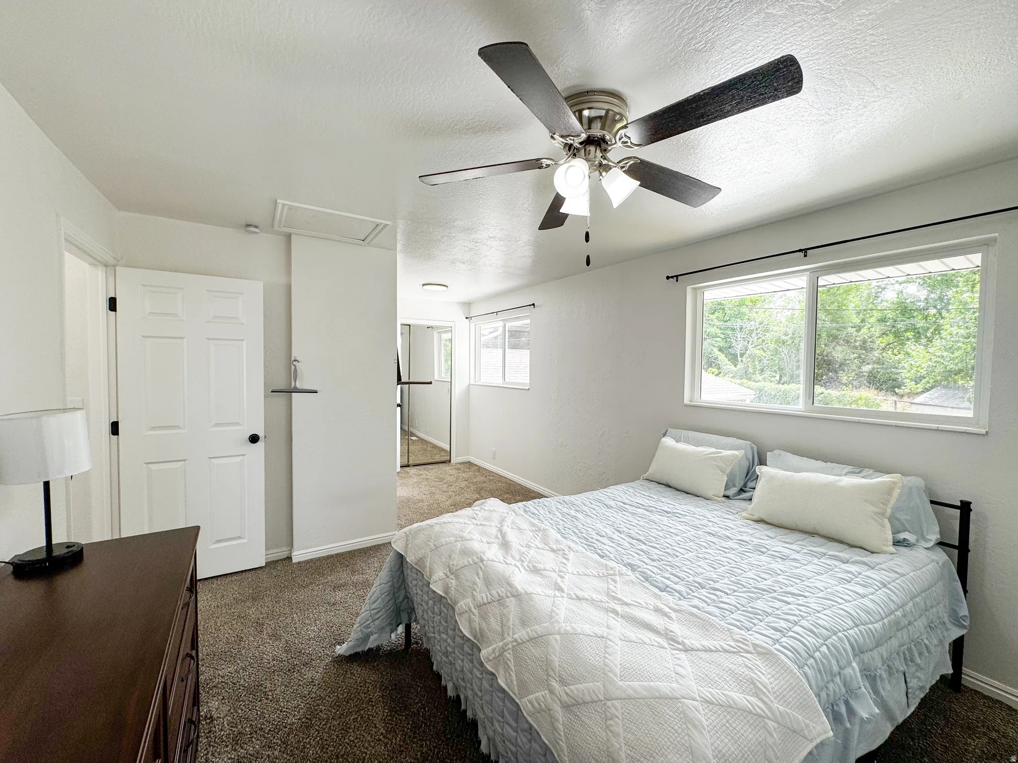 Ceiling fan with integrated lighting, multiple windows with dark-finish curtain rods, white interior doors, and textured wall finishes