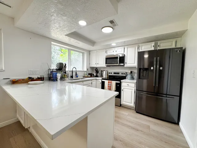 Kitchen featuring white cabinetry, light-toned wood-finish flooring, white countertop surfaces, and stainless-steel appliances