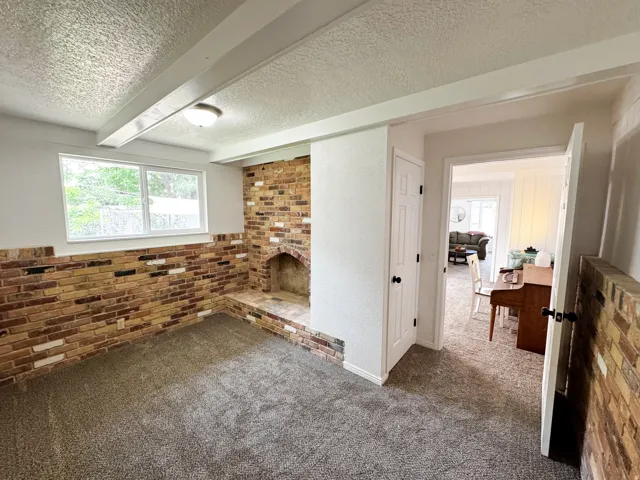 Brick accent wall with an integrated fireplace and hearth, wall-to-wall carpeting, and a dual-pane window