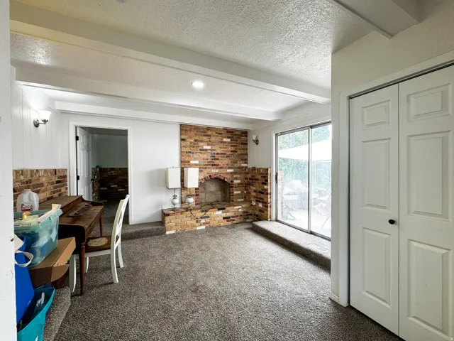 Exposed brick fireplace, sliding glass door, white bi-fold closet doors, wall paneling, and ceiling beams