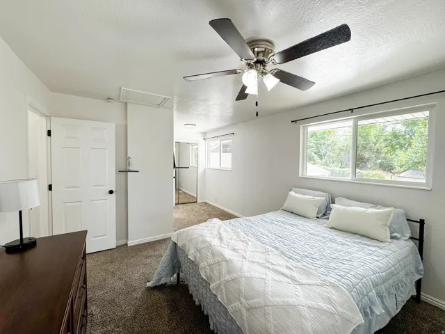 Ceiling fan with integrated lighting, multiple windows with dark-finish curtain rods, white interior doors, and textured wall finishes
