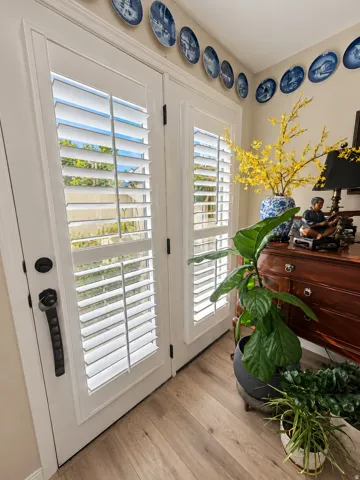 White double French doors with interior plantation shutters, black hardware, and wood-finish flooring