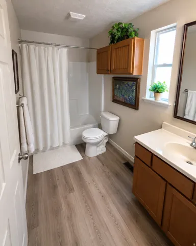 Bathroom featuring wood-finish flooring, a white vanity with an integrated sink, a built-in tub and shower combination, and a window providing natural light