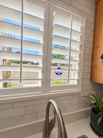 White plantation shutters, subway tile backsplash, Quartz solid surface countertop, and a gooseneck faucet