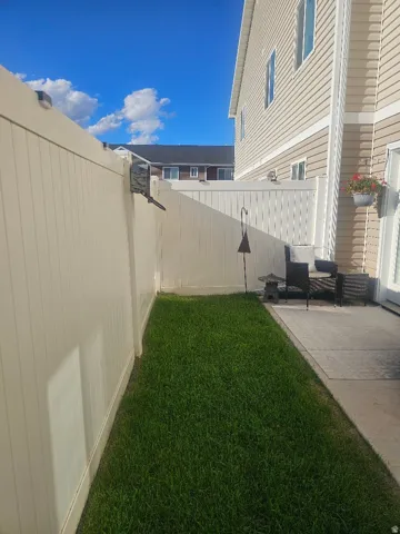Private patio with concrete surfacing, adjacent grassy area, and vinyl fencing