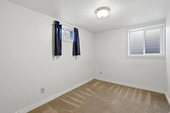 Carpeted flooring, white painted walls, two windows with white frames, and a flush-mount ceiling light fixture