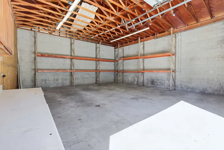 Spacious interior featuring exposed wood-beam ceiling, concrete block walls, industrial shelving, and concrete flooring
