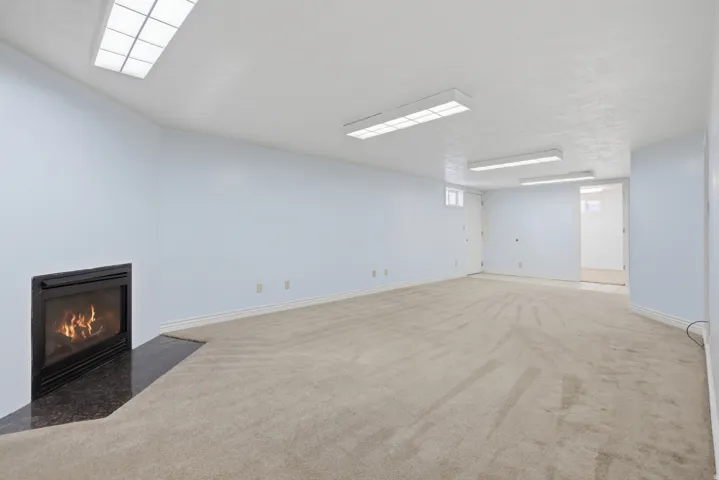 Spacious carpeted room featuring a built-in fireplace with a dark stone hearth, light blue walls, and multiple ceiling-mounted light fixtures