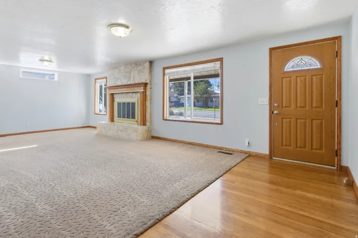 Stone-surround fireplace with a wood mantle, wood-frame windows, wood-panel entry door with decorative glass, and wood flooring