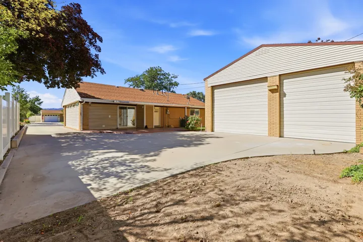 Expansive concrete driveway leading to a two-car garage with roll-up doors, and an additional detached garage structure