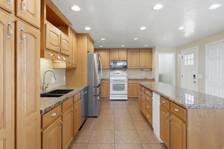 Kitchen featuring wood cabinetry, granite-finish countertops, stainless steel appliances, and recessed lighting