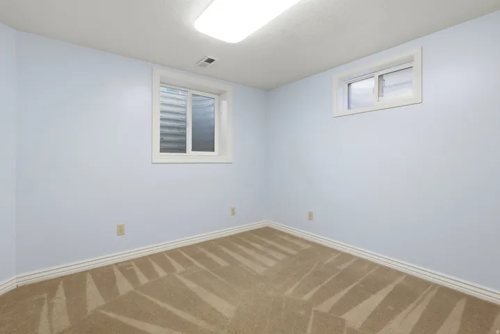 Wall-to-wall patterned carpeting, white window trim, and overhead flush-mount lighting