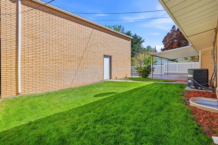 Expansive lawn area with a brick exterior building, a covered carport structure, and a white fence