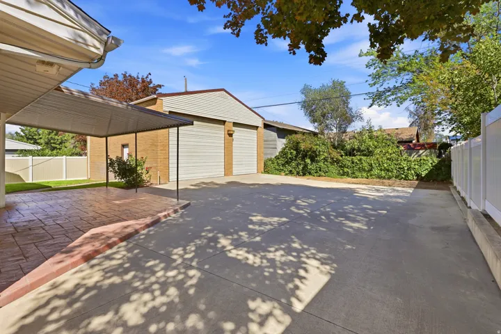 Expansive concrete driveway, two-car garage with roll-up doors, covered patio with stamped concrete, and perimeter fencing