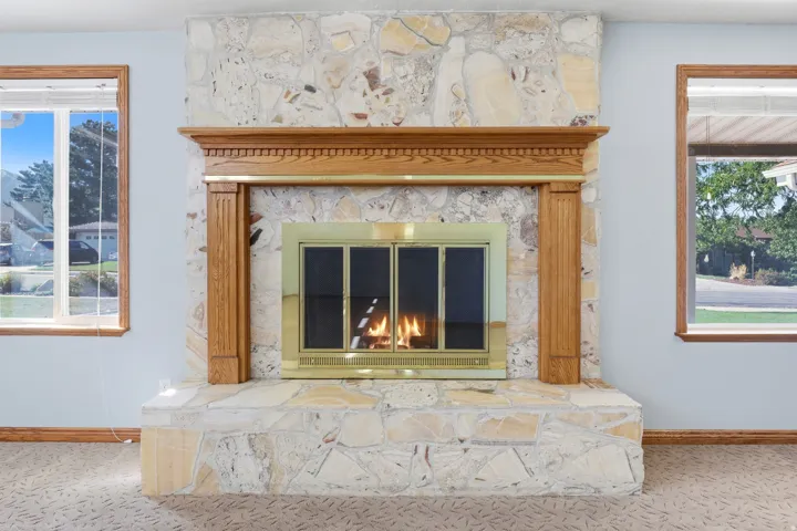 Stone-clad fireplace with a brass firebox, detailed wood mantel, and wood-framed windows