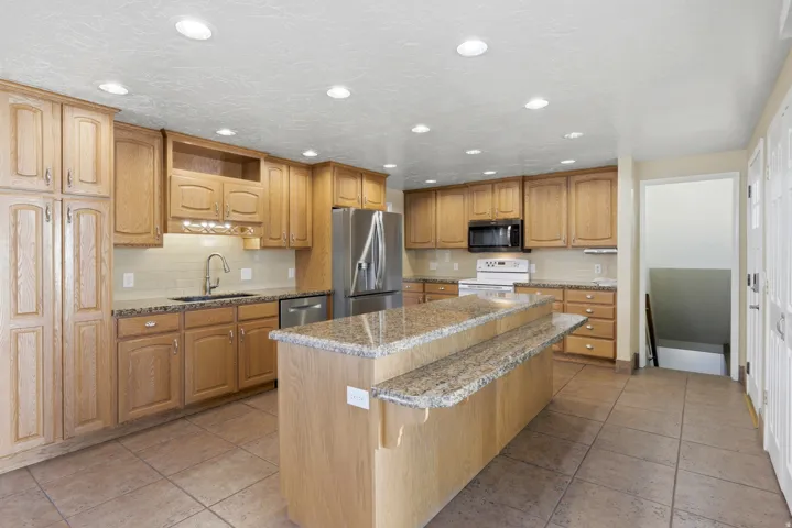 Kitchen featuring a two-tiered island, light wood cabinetry, recessed lighting, tile flooring, and stainless steel appliances