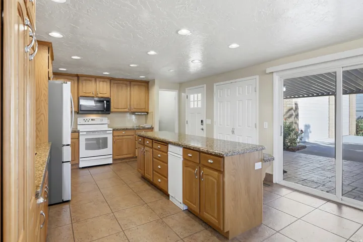 Kitchen featuring wood cabinetry, a center island with countertop, tile flooring, and white appliances