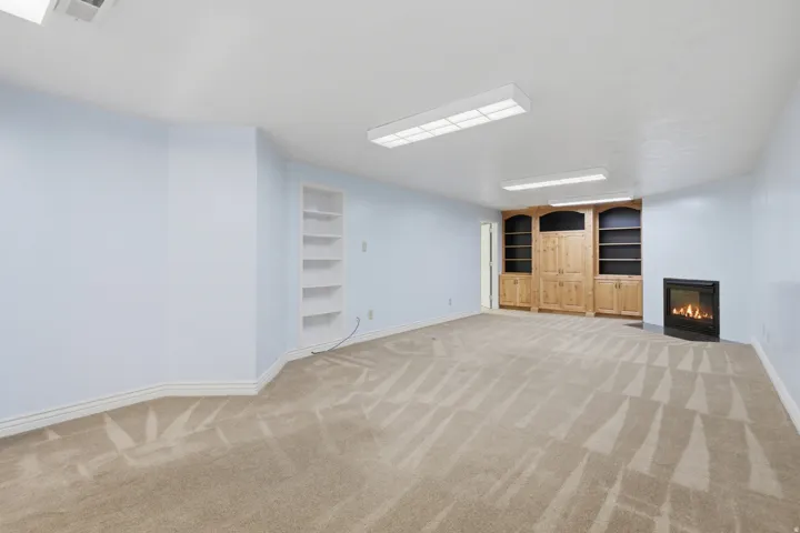 Recessed fireplace, built-in shelving, wood-finish cabinetry, light blue wall paint, and patterned carpet flooring