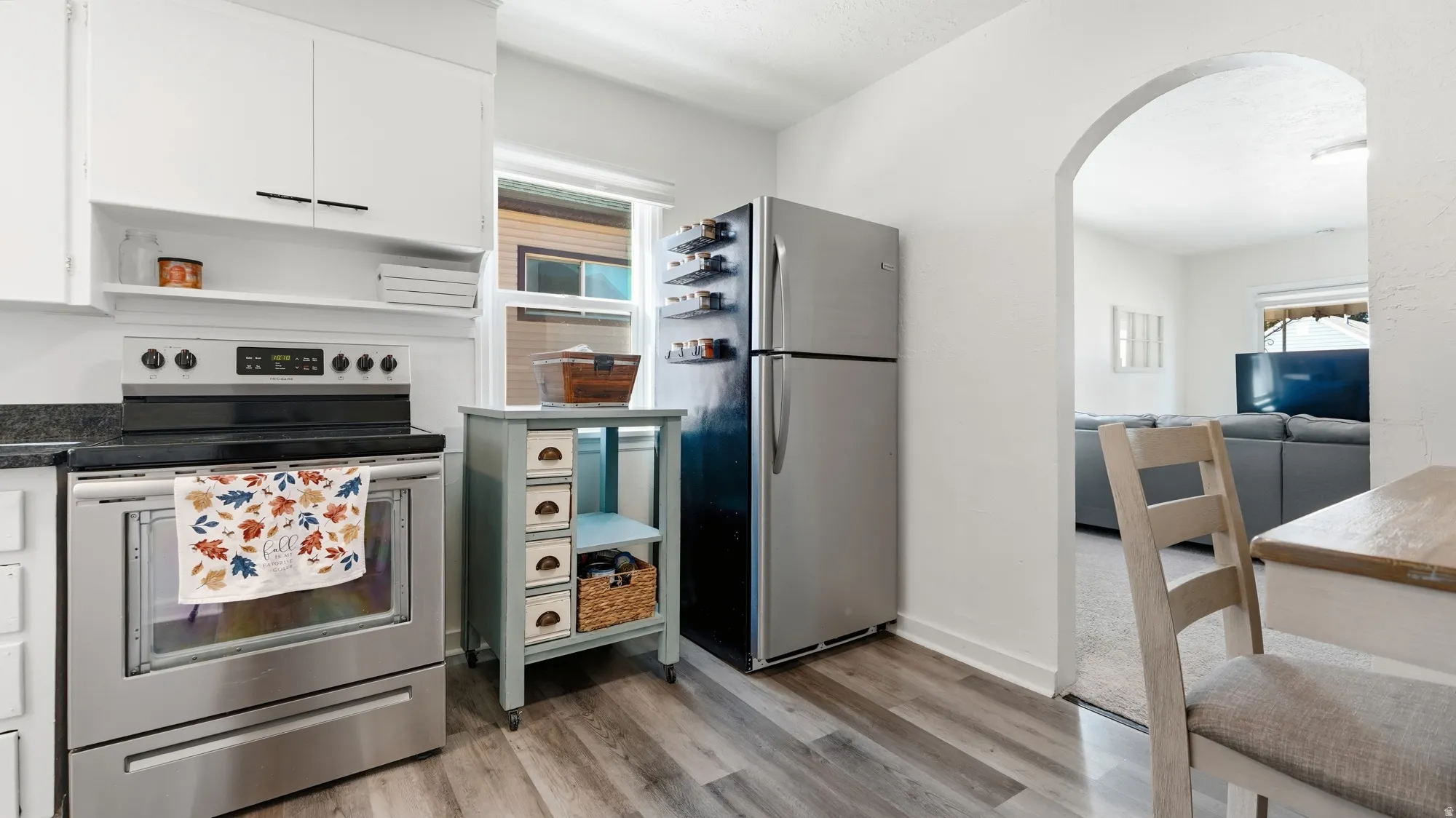 Kitchen featuring wood-finish flooring, stainless steel appliances, dark countertops, white cabinetry, and an arched doorway