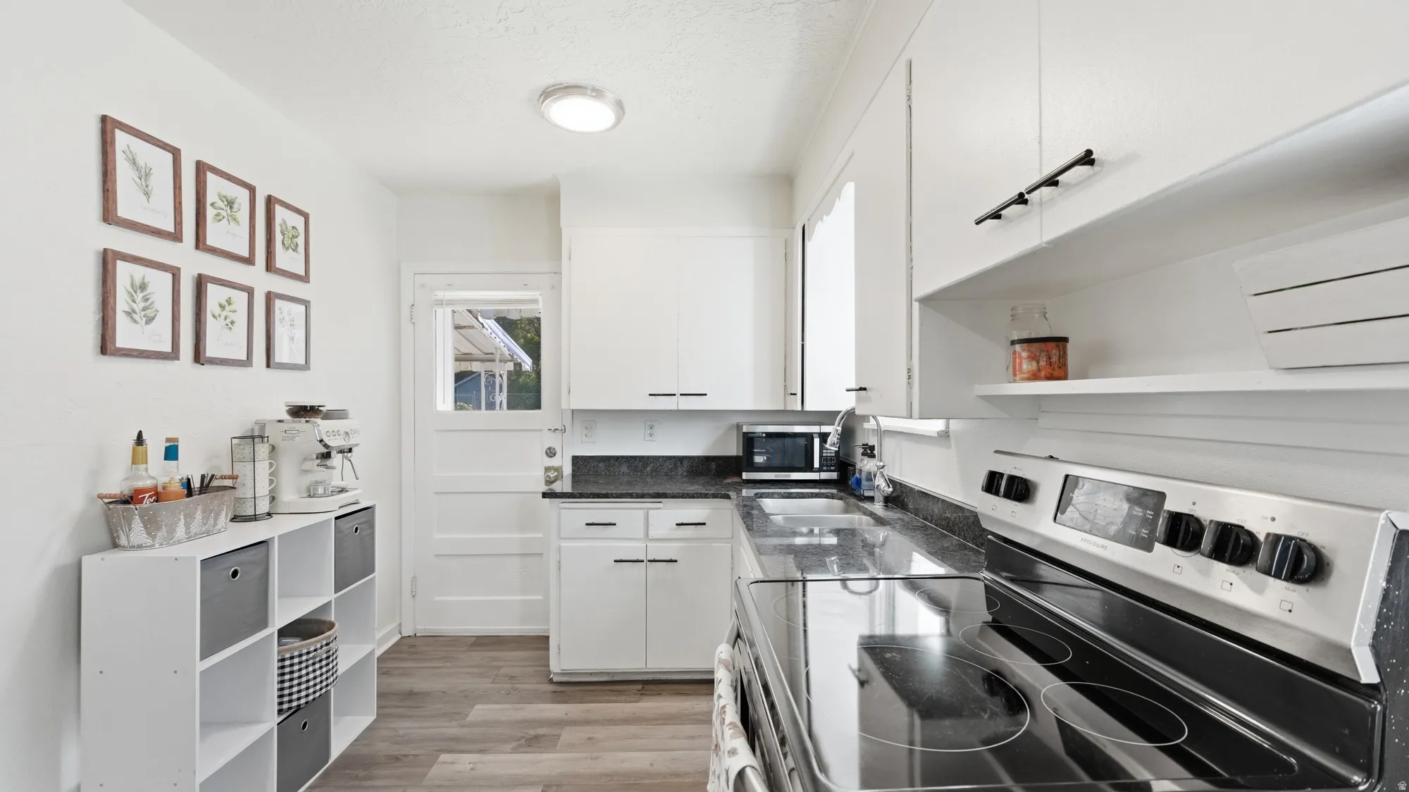 Modern kitchen featuring white cabinetry, dark countertops, wood-finish flooring, a stainless steel range, and a built-in sink
