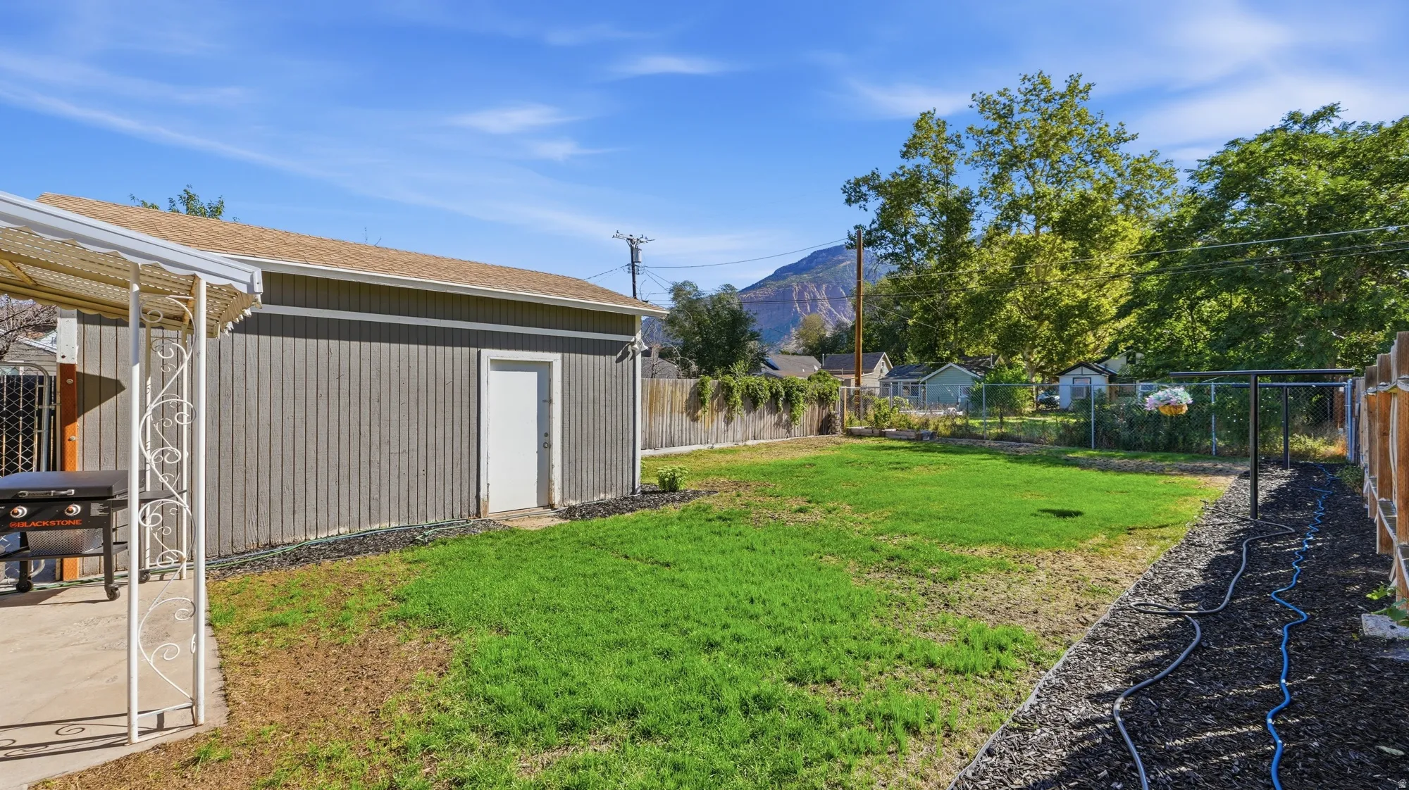 Expansive backyard featuring a green lawn, wood fencing, and a separate structure with a white entry door