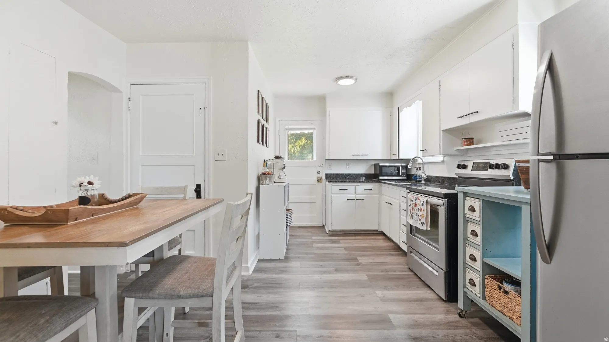 Open-concept kitchen and dining area featuring wood-finish flooring, white cabinetry, dark countertops, and stainless steel appliances