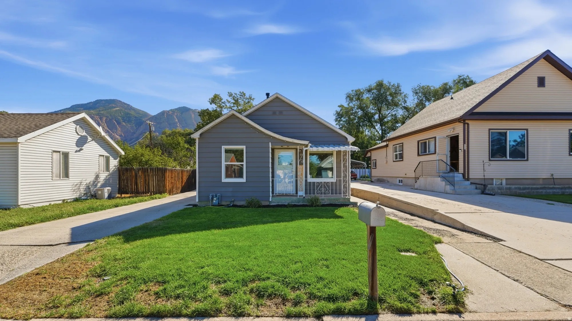 Blue siding exterior with white trim, covered front porch, concrete driveway, and a manicured front lawn