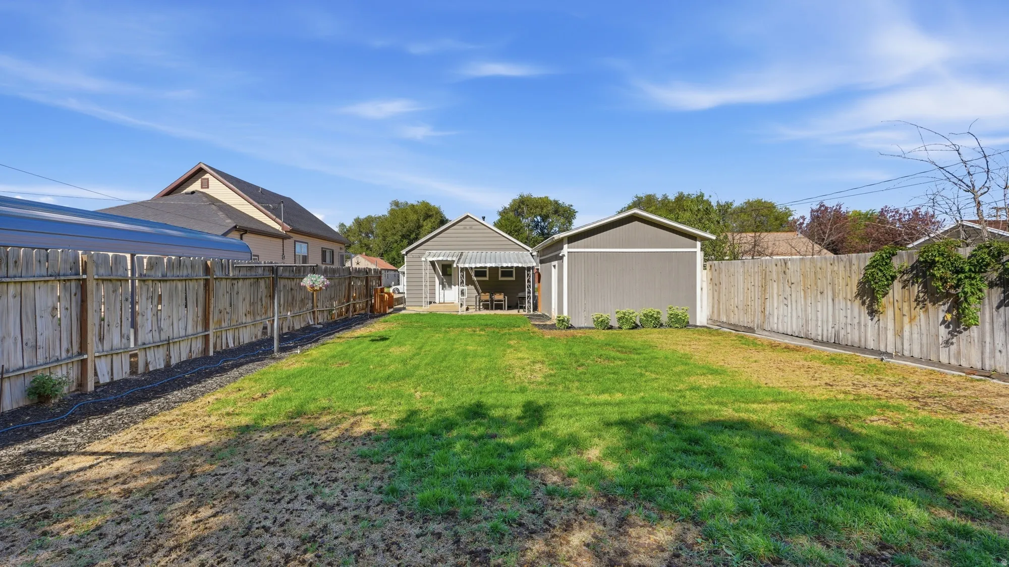 Expansive backyard with a manicured lawn, full privacy fencing, and a detached auxiliary building