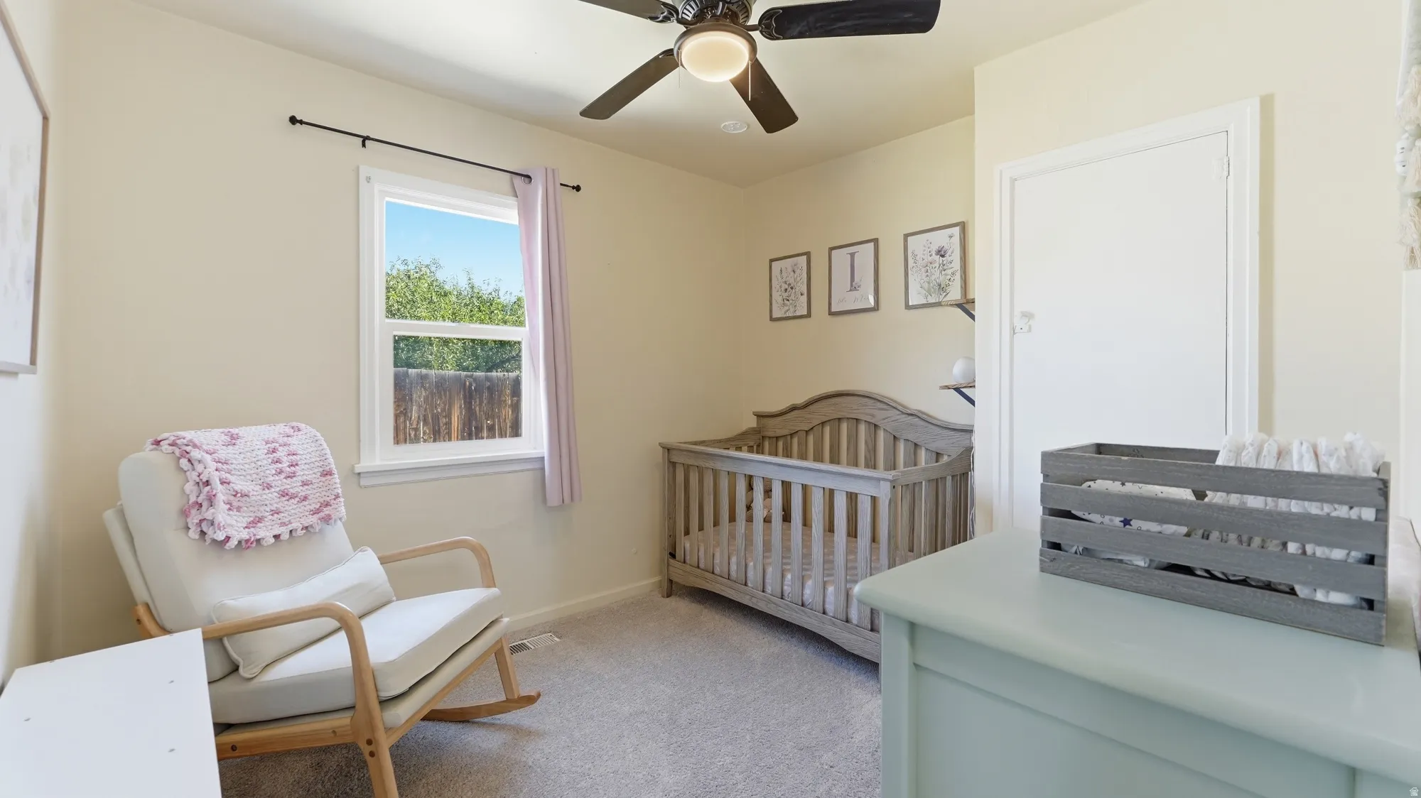 Room featuring a ceiling fan, carpet flooring, and a single window with a privacy fence outside