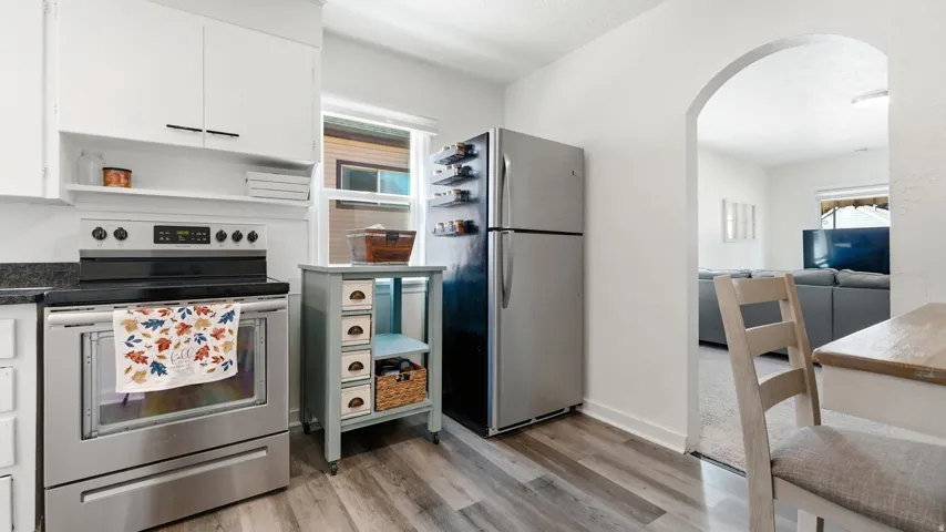 Kitchen featuring wood-finish flooring, stainless steel appliances, dark countertops, white cabinetry, and an arched doorway