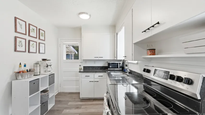 Modern kitchen featuring white cabinetry, dark countertops, wood-finish flooring, a stainless steel range, and a built-in sink