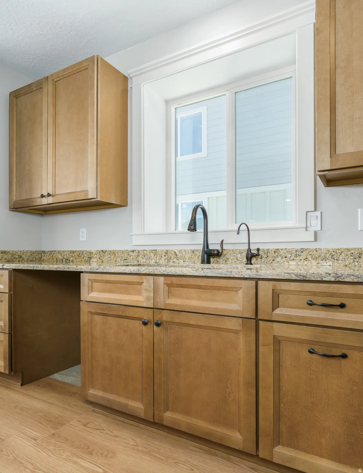 Light wood-finish cabinetry with black hardware, granite-style countertops, wood-finish flooring, and a black gooseneck faucet