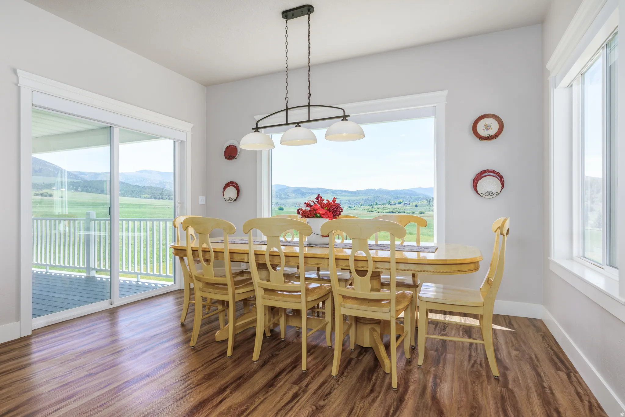 Wood-finish flooring, white trim, sliding glass door to exterior, large window, and ceiling-mounted chandelier