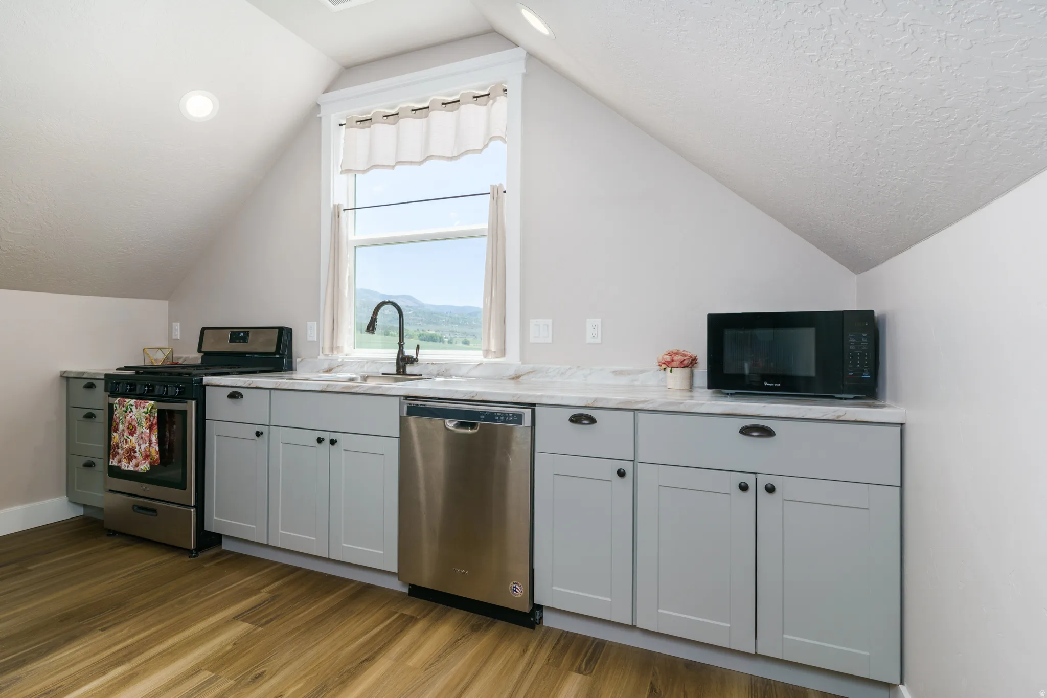 Compact kitchen featuring light gray cabinetry, stainless steel appliances, a black gooseneck faucet, and wood-finish flooring