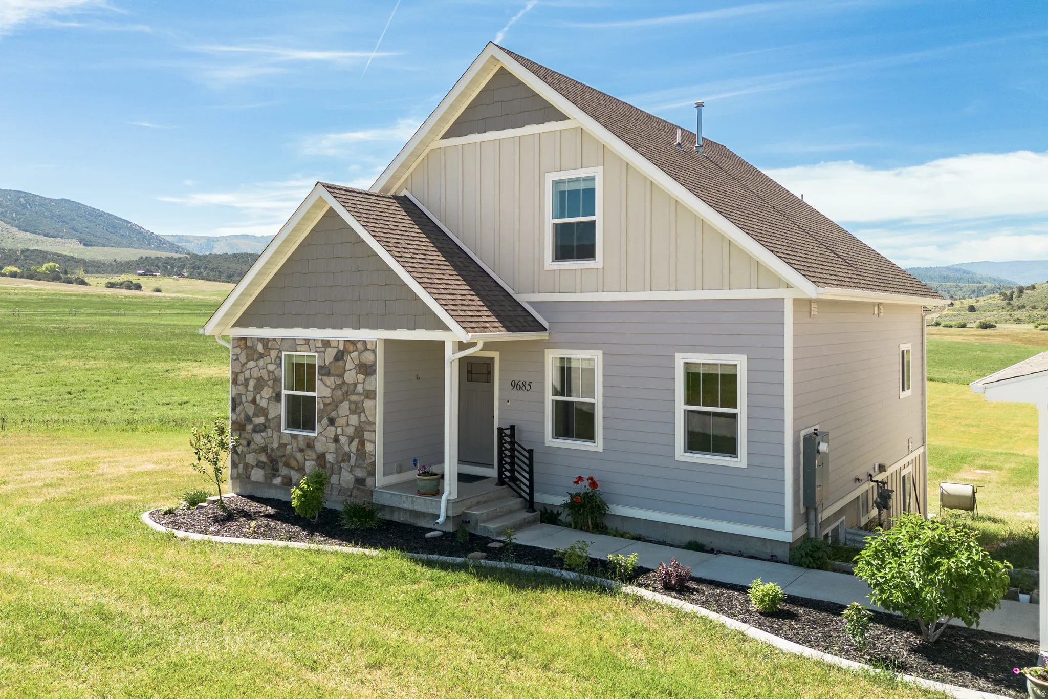 Stone and siding exterior with a covered entry, gabled rooflines, and a manicured front lawn with plantings