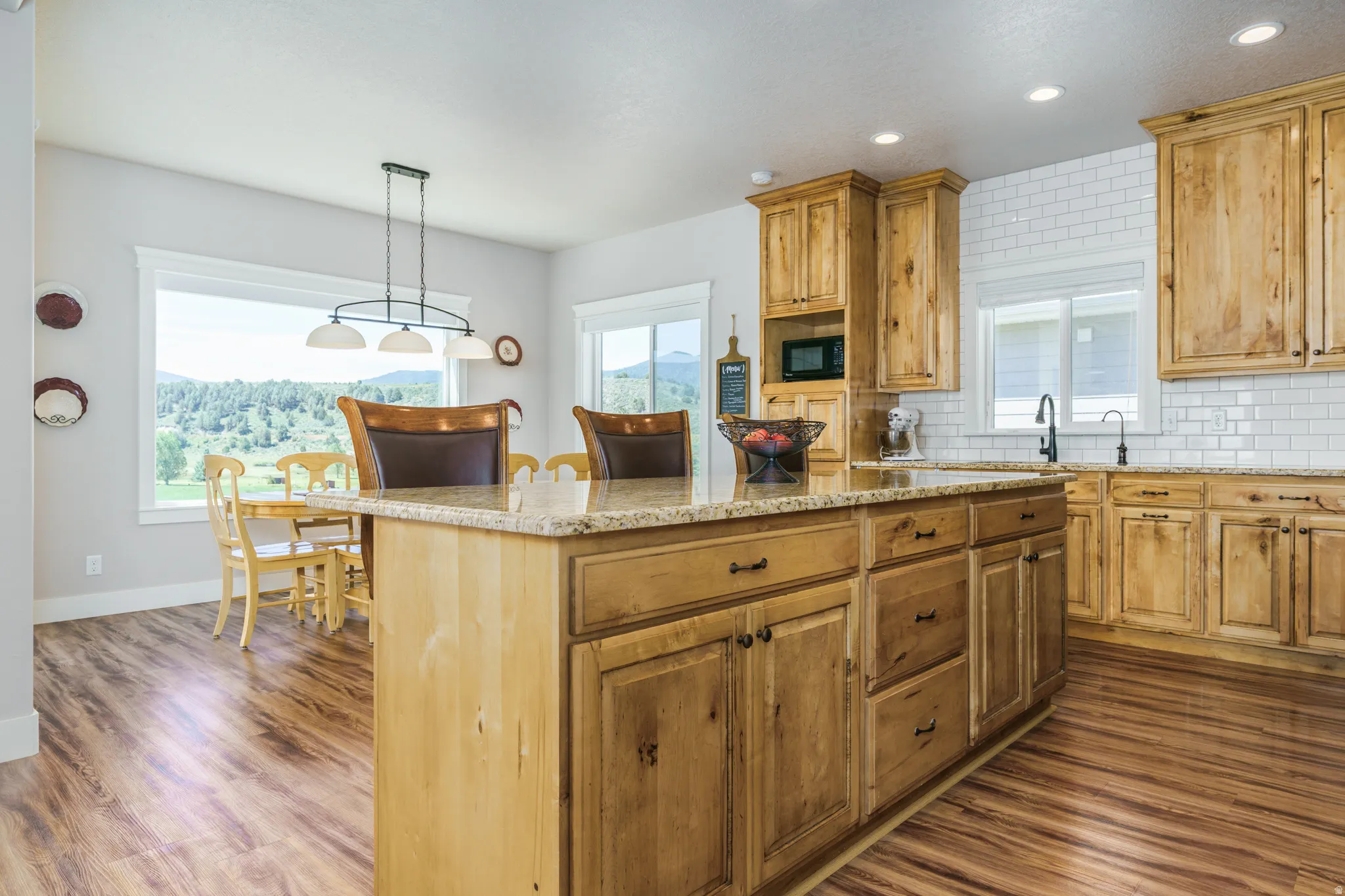 Kitchen featuring wood-finish flooring, natural wood cabinetry, white subway tile backsplash, and a large central island with a stone countertop