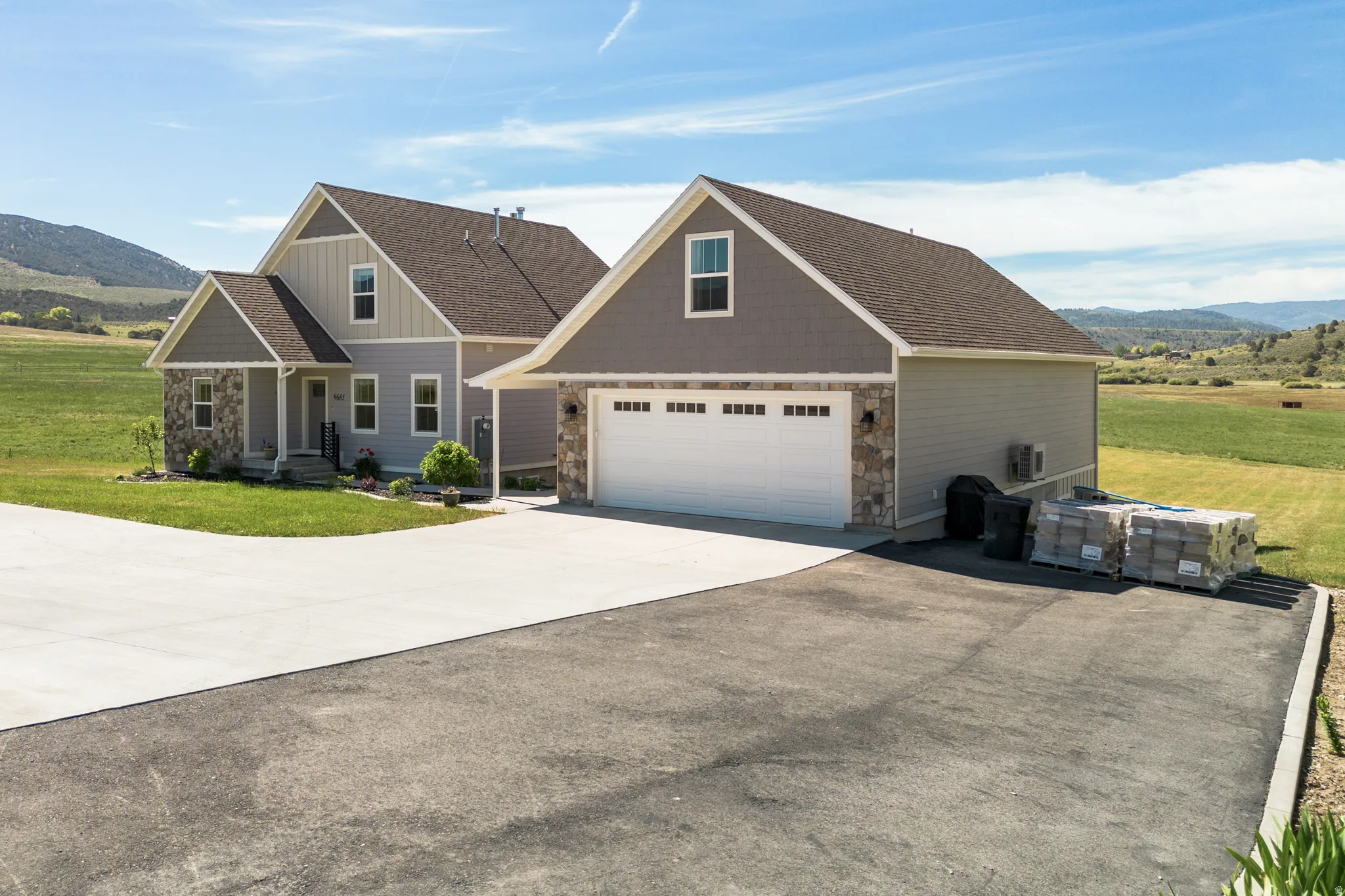 Two-story residence featuring light gray siding, stone accents, a covered front porch, and an attached two-car garage