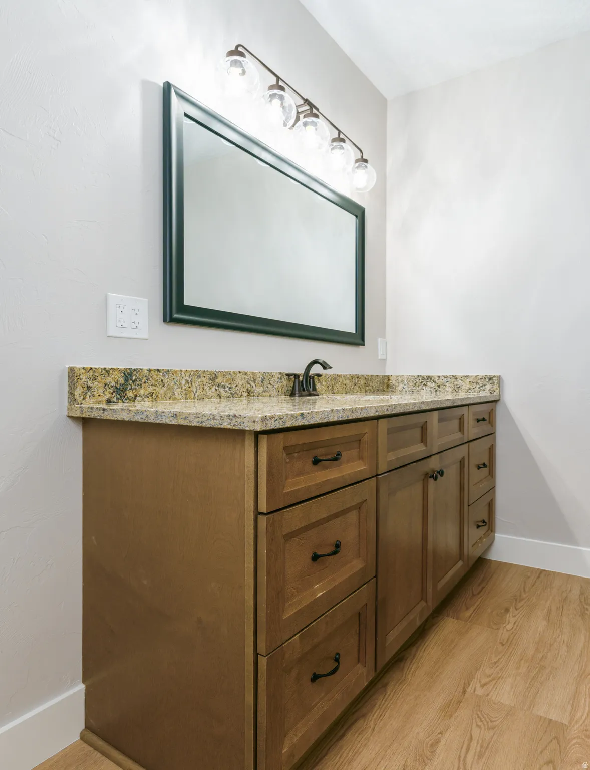 Wood-finish flooring with a multi-drawer vanity, stone-finish countertop, and decorative lighting fixture