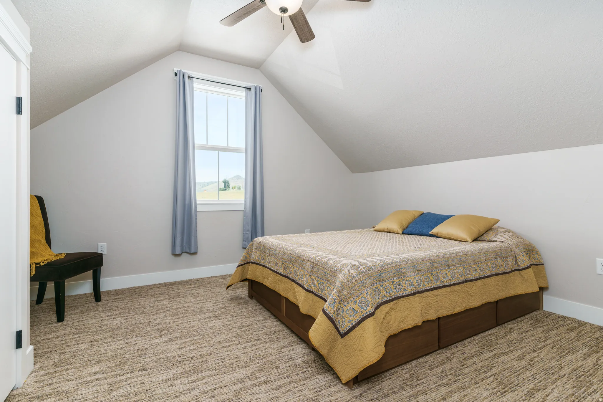 Sloped ceilings, window with white trim, ceiling fan with integrated lighting, and textured carpeting