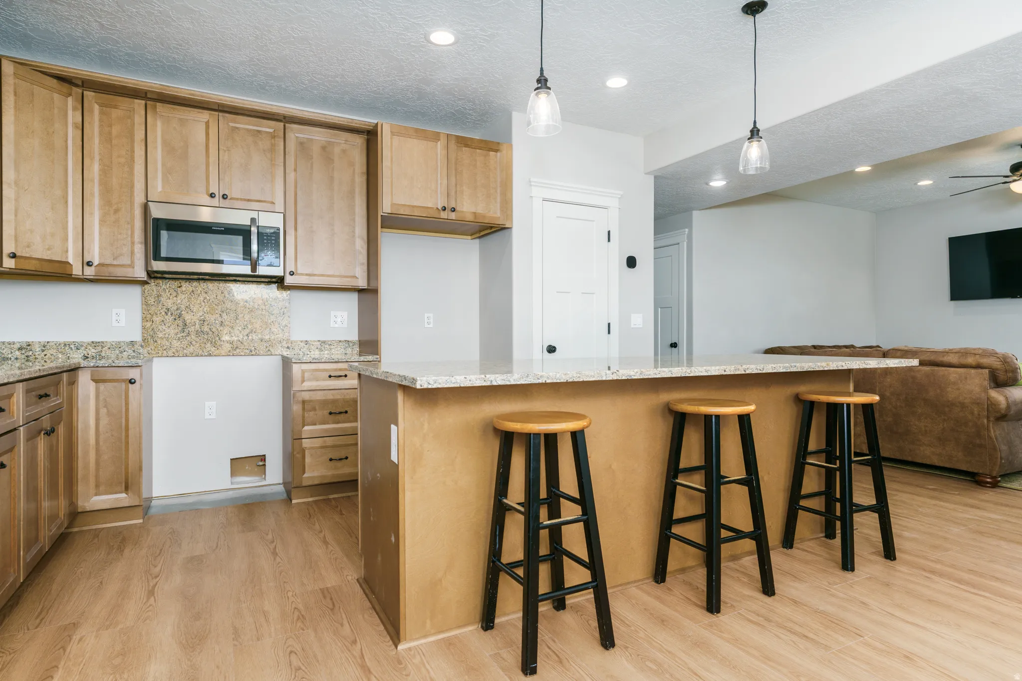Kitchen featuring light wood cabinetry, stone countertops, stainless steel microwave, and wood-finish flooring