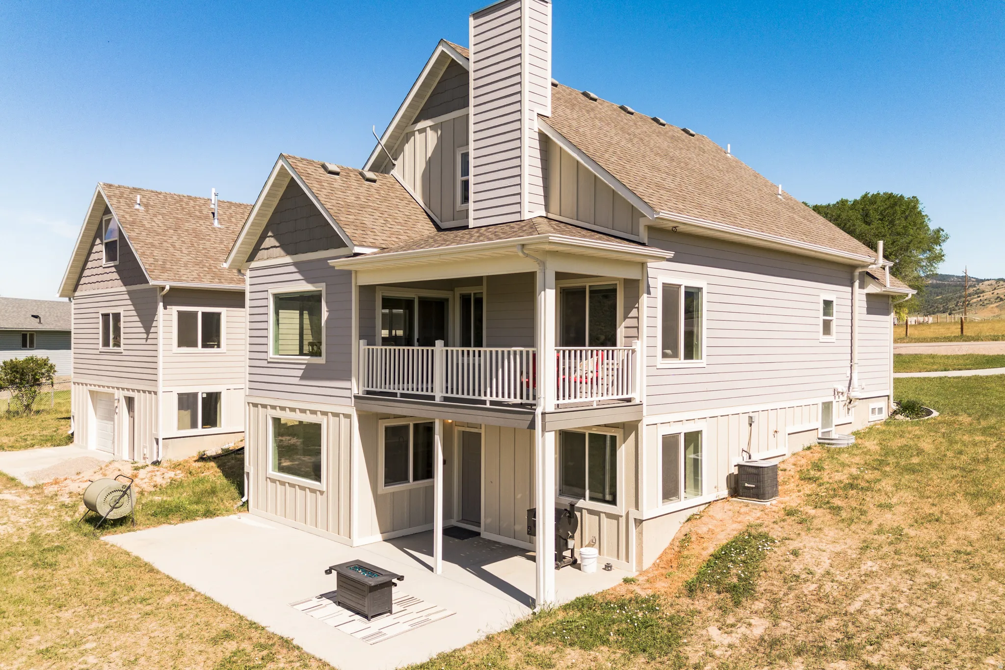 Multi-level property exterior featuring siding, an upper-level balcony, lower-level patio, and attached chimney