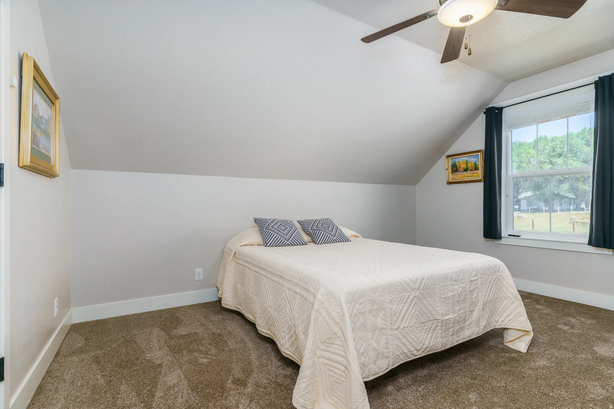 Sloped ceiling room featuring a window with exterior scenery, overhead ceiling fan with lighting, and plush carpeting